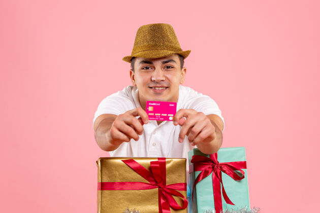 快乐年轻人在圣诞节前后的正面图 粉红色的墙上挂着一张银行卡年轻男性举行快乐
