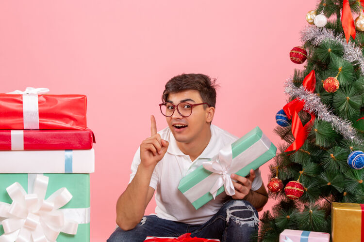 情侣年轻人围着礼物和粉红色墙上的圣诞树的正视图前面年轻男性礼品盒