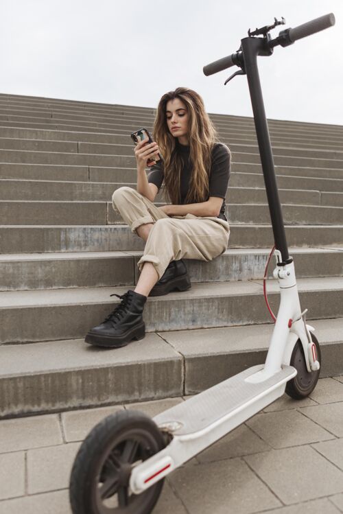 电动年轻女子正在浏览她的手机滑板车女子垂直