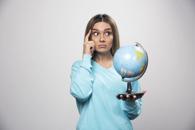 年轻人穿着蓝色运动衫的金发女孩手里拿着一个地球仪 仔细地思考着 努力地记住目的地旅行地球