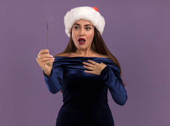她自己一个穿着蓝色连衣裙 戴着圣诞帽的年轻漂亮女孩 手里拿着闪闪发光的东西 把自己孤立在紫色的墙上摆圣诞节年轻人
