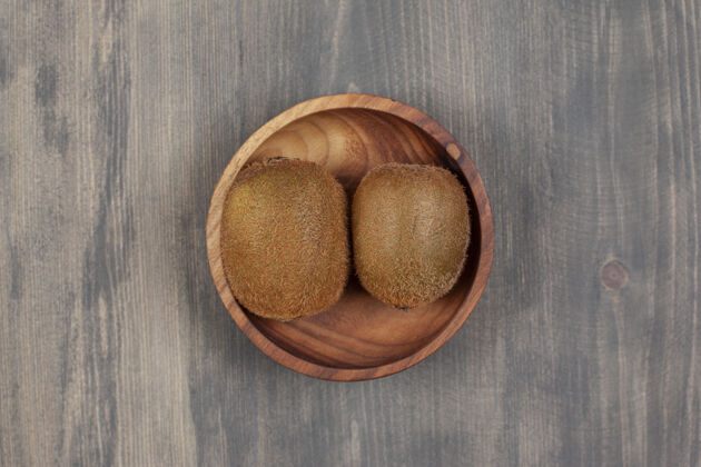 吃木桌上放着一个木碗和两个新鲜的猕猴桃高质量的照片水果多汁甜食