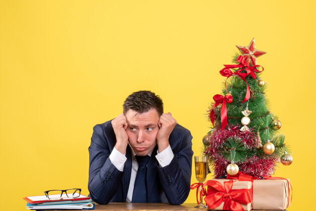桌子前视图：体贴的男人坐在圣诞树旁的桌子旁 黄色的礼物专业人士体贴的男人树