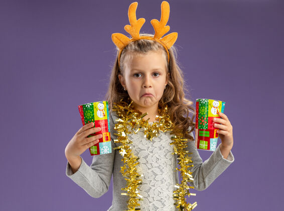 头发悲伤的小女孩戴着圣诞发箍 脖子上戴着花环 手里拿着蓝色背景上孤立的圣诞杯子女孩杯子圣诞节