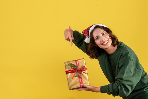 Covid黄色墙上拿着小圣诞礼物的年轻女子的正面图微笑聚会人