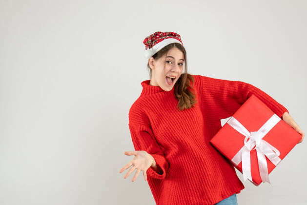 礼物戴着圣诞帽的快乐女孩拿着礼物站在白色的地板上人休闲成人
