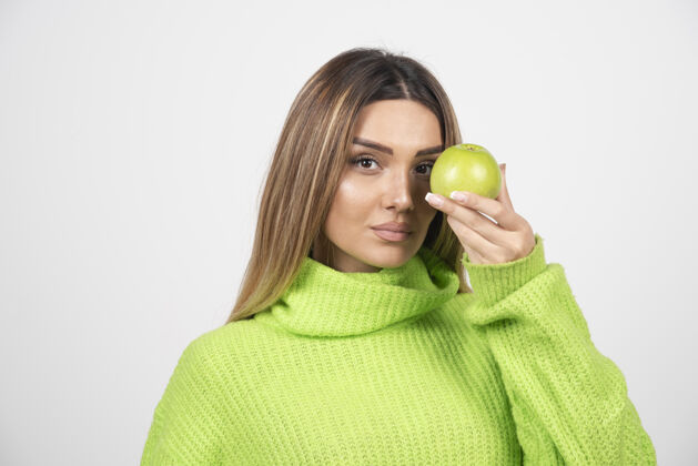 举行穿着绿色t恤的年轻女子手里拿着一个苹果营养吃食物