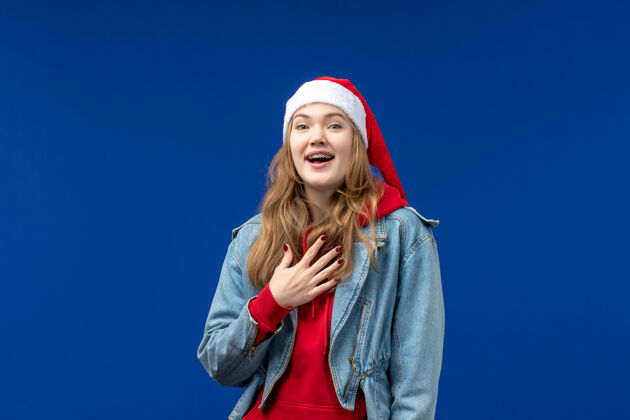 微笑正面图蓝色背景上戴着红色圣诞帽的年轻女性感慨圣诞假期人物年轻年轻女性