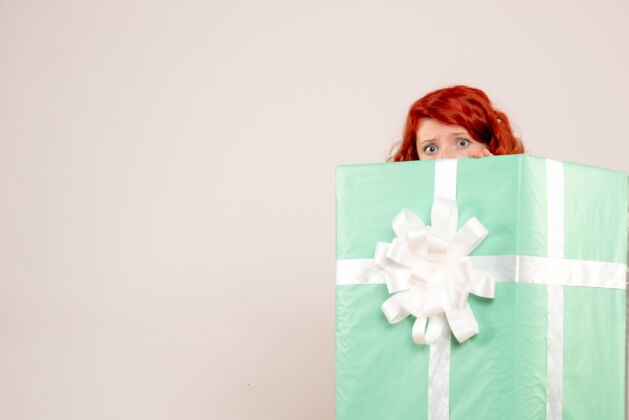 人年轻女子隐藏在白色墙上的圣诞礼物内的正面视图里面礼物快乐