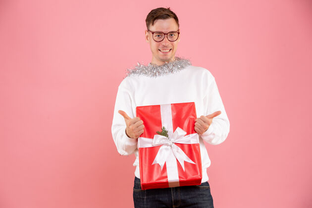 粉色一个年轻人在粉红色的墙上拿着圣诞礼物的正面图盒子圣诞节年轻