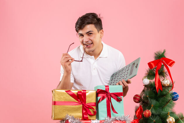 圣诞节圣诞节前后的年轻人手持计算器站在粉红色的墙上礼品盒十二月礼物