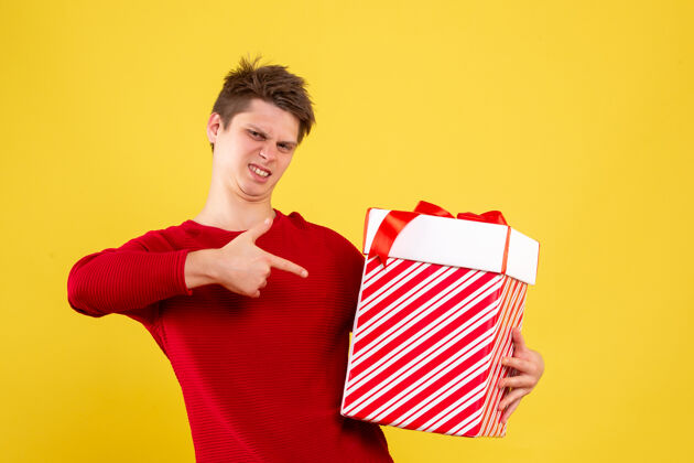 成人黄色墙上拿着圣诞礼物的年轻人的正视图礼物盒礼物情感