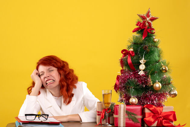 圣诞节女工人坐在桌子后面 手里拿着圣诞礼物和黄色的圣诞树女工人人坐着