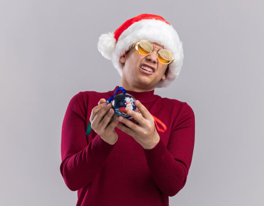 圣诞节遗憾的是那个戴着圣诞帽戴着眼镜拿着圣诞树球的年轻人被隔离在白色背景上树球抱着