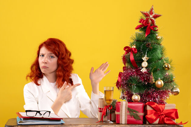 女女工人坐在桌子后面 手里拿着圣诞礼物和黄色的圣诞树黄色成人礼物