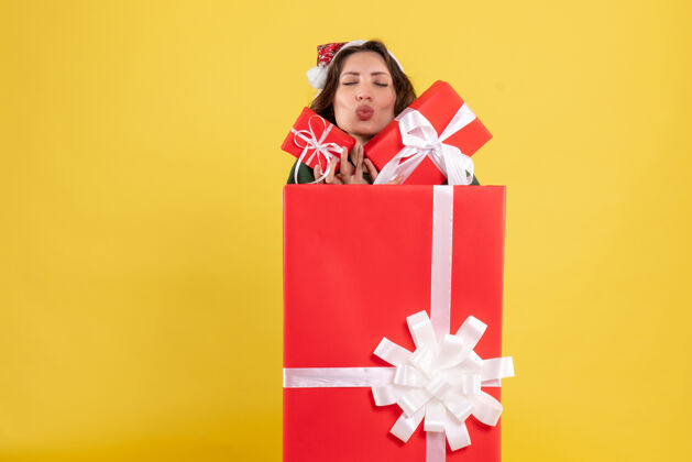 丝带站在盒子里的年轻女子的正面图 黄色的墙上有圣诞礼物圣诞节前面站立