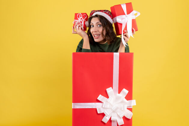 礼物站在盒子里的年轻女子的正面图 黄色的墙上有圣诞礼物年轻女性购物礼物