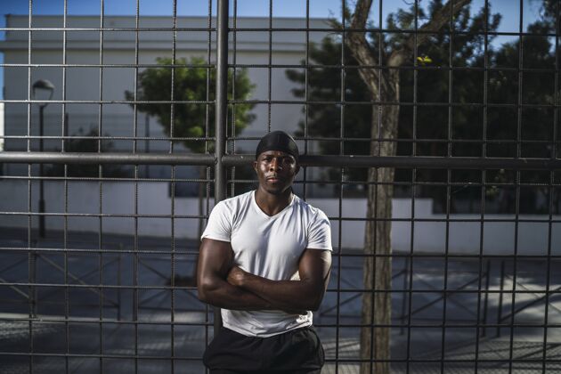 运动一个穿白衬衫的非洲裔美国男性斜靠在篱笆上双臂交叉的浅焦镜头健身人男人