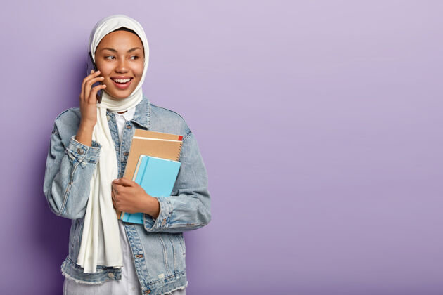 积极面带微笑的阿拉伯女人打电话聊天 看向一边 通过手机与团友讨论最新消息举行优雅高兴