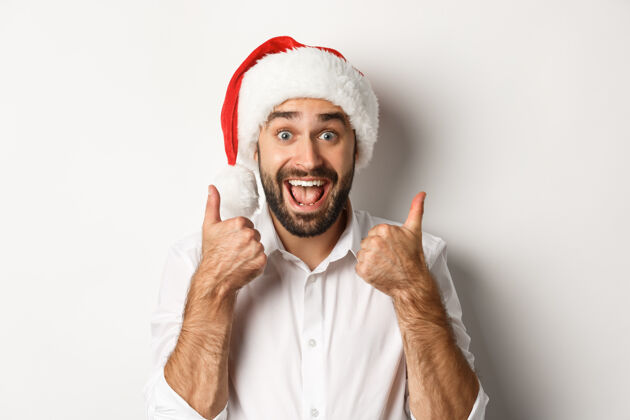 圣诞老人派对 寒假和庆祝的概念男人享受圣诞节 戴圣诞帽和显示拇指与兴奋的脸圣诞节庆祝兴奋