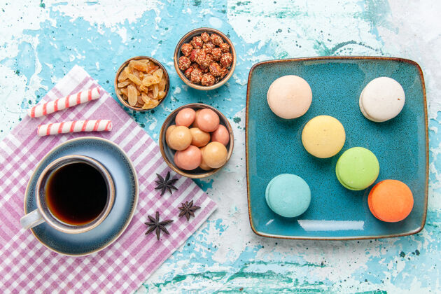 查看俯瞰一杯咖啡 配上法式马卡龙葡萄干和淡蓝色表面的果酱蛋糕烘焙甜甜的糖派饼干葡萄干烘烤咖啡
