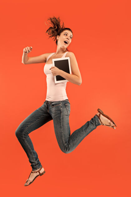 无线年轻女子跳过蓝色工作室使用笔记本电脑或平板电脑小玩意 而跳跃平板电脑女人携带