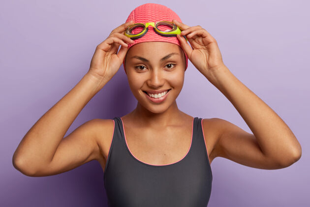 高兴快乐的非洲裔美国妇女的头像手放在护目镜上 对着镜头灿烂地微笑游泳帽子力量