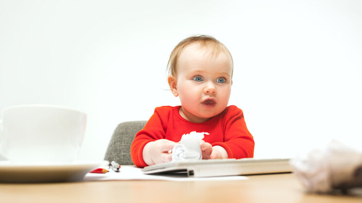 可爱快乐的小女婴坐在一个白色的工作室里 用现代电脑或笔记本电脑的键盘隔离电脑桌子键盘
