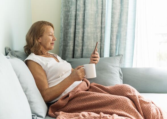 杯子大流行期间 家中的老妇人一边喝咖啡一边用智能手机防护女人隐居