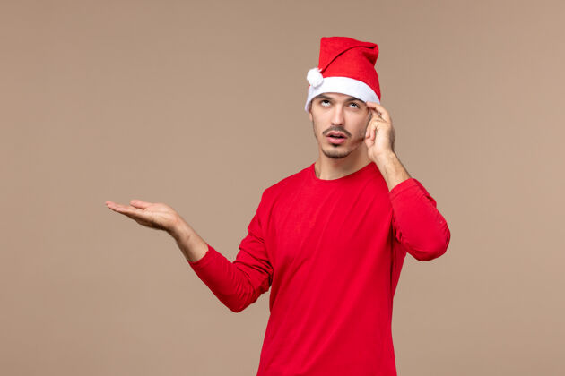 休闲正面图年轻男性思考着一个棕色背景的节日圣诞节的情绪快乐节日年轻男性