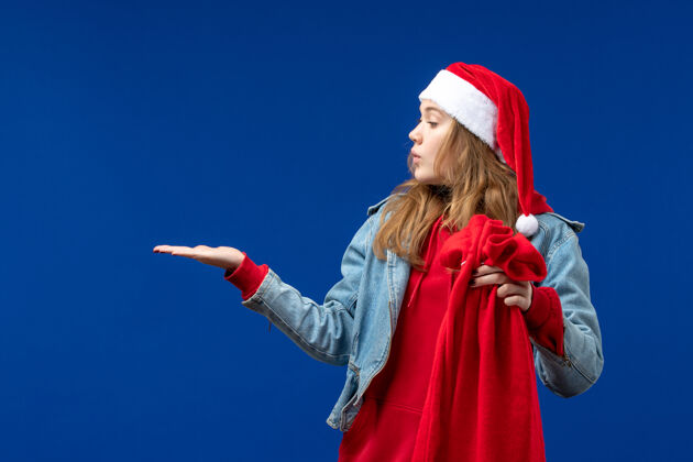 女性前视图年轻女性拿着蓝色背景上的礼物圣诞情感袋人人圣诞节