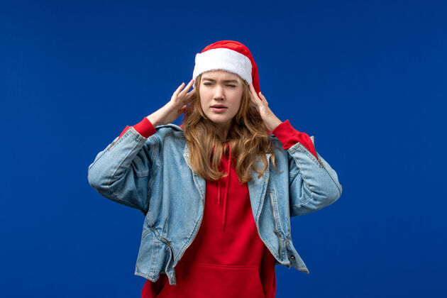 肖像正面图蓝色背景上有头痛的年轻女性圣诞情感色彩帽子漂亮圣诞节