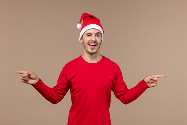 背景正面图年轻男性在棕色背景上眨眼情感节日圣诞节微笑微笑工作室