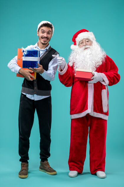 礼物圣诞老人与年轻男性和礼物在蓝色墙上的正面视图前面成人圣诞快乐