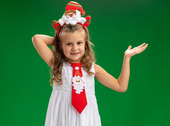 边高兴的小女孩戴着圣诞发箍与领带点 手在一边孤立的绿色背景与复制空间快乐领带箍