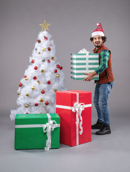 圣诞礼物年轻的男性在灰色的圣诞礼物周围礼物庆祝盒子