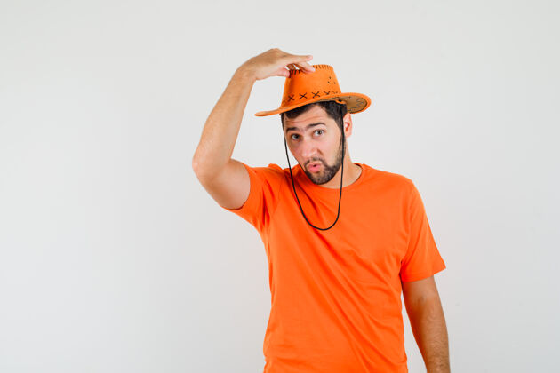 工作室在橘色t恤前视图中 年轻人正试图摘下帽子帅气时尚人