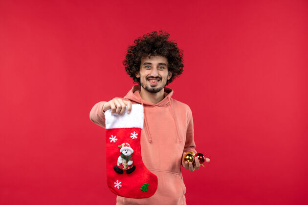 时尚红墙上拿着玩具和袜子的年轻人的正视图脸模型圣诞节