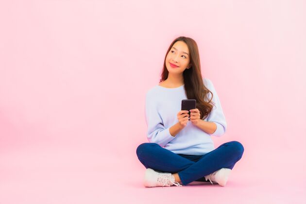 兴奋肖像美丽的亚洲年轻女子在粉色隔离墙上使用智能手机女学生智能短信
