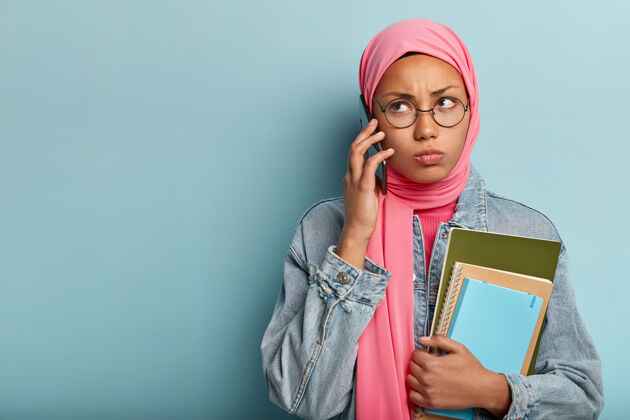 举行严肃的阿拉伯女人通过手机打电话 注意力放在一边 表情暴躁 戴着圆眼镜种族牛仔伊斯兰