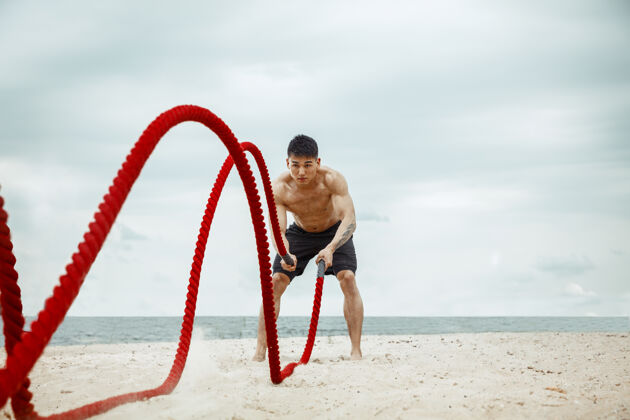 教练年轻健康的男子运动员在海滩上做深蹲力量健美强壮