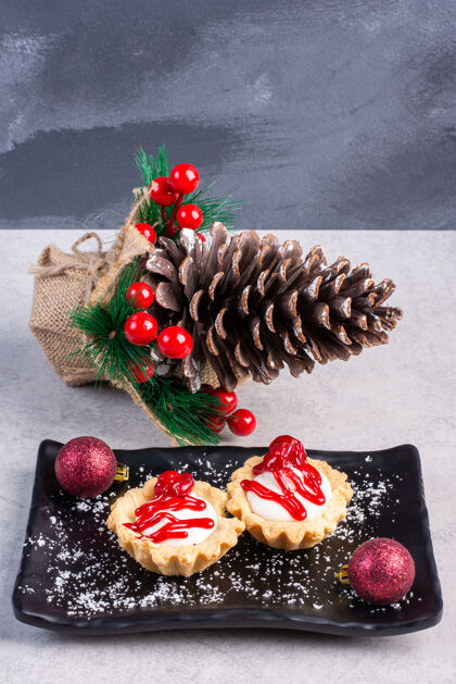 甜点把草莓酱纸杯蛋糕放在一个黑色的盘子里 在大理石表面绑上圣诞装饰品美味纸杯蛋糕糖