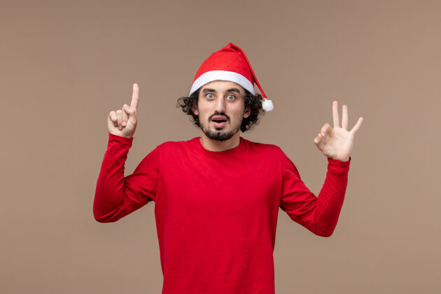 年轻正面图：穿着棕色背景圣诞斗篷的年轻人圣诞节情绪背景脸欢乐