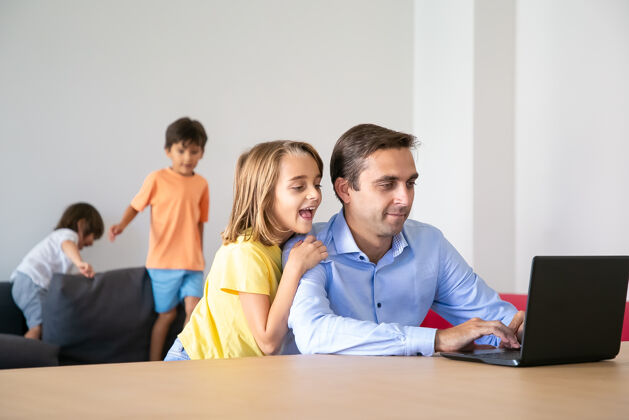生活可爱的女孩看着笔记本电脑屏幕 拥抱着爸爸白人中年爸爸在家工作时 可爱的孩子在沙发上玩耍童年 父亲和数字技术的概念可爱儿子爸爸
