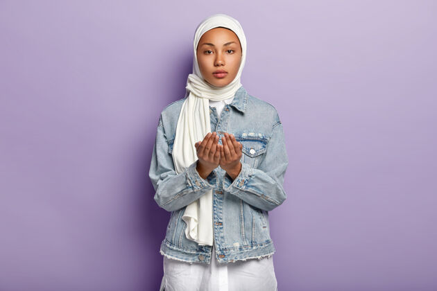 严肃手势和祈祷概念严肃的黑皮肤女性举手祈祷 祈求某事 戴围巾和牛仔夹克 隔离在紫色墙壁上宗教概念头混合面伊斯兰
