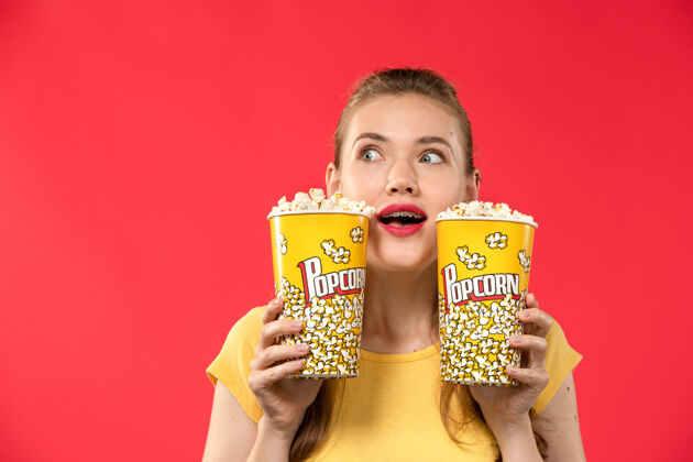 杯子正面图年轻女性在电影院拿着爆米花包在浅红的墙上电影院看女性趣味电影容器年轻女性咖啡杯