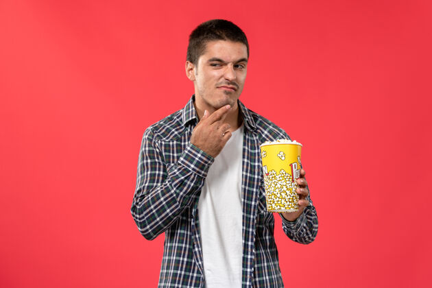 年轻人正面图年轻男性手持爆米花包在浅红墙电影院看男性电影浅红色男性电影