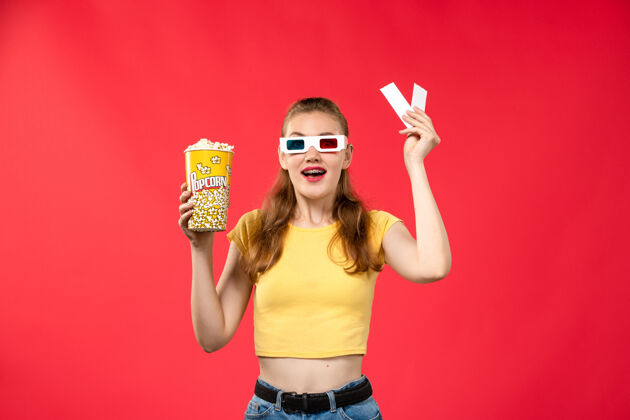 肖像正面图年轻女子在电影院里拿着爆米花和红墙电影院的票女彩色年轻人电影视图