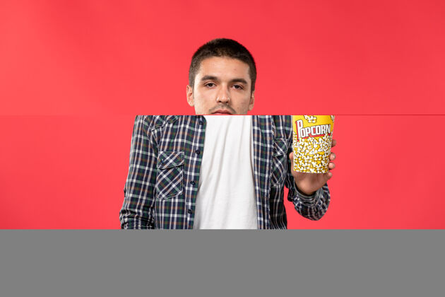 爆米花正面图年轻男子手持爆米花包在红墙电影院男性包装年轻