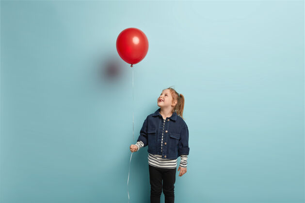 条纹生日派对和童年概念姜黄色头发的快乐小孩横拍 在红色气球上快乐地向上看 穿着时髦的衣服 站在蓝色的墙上小高兴夹克